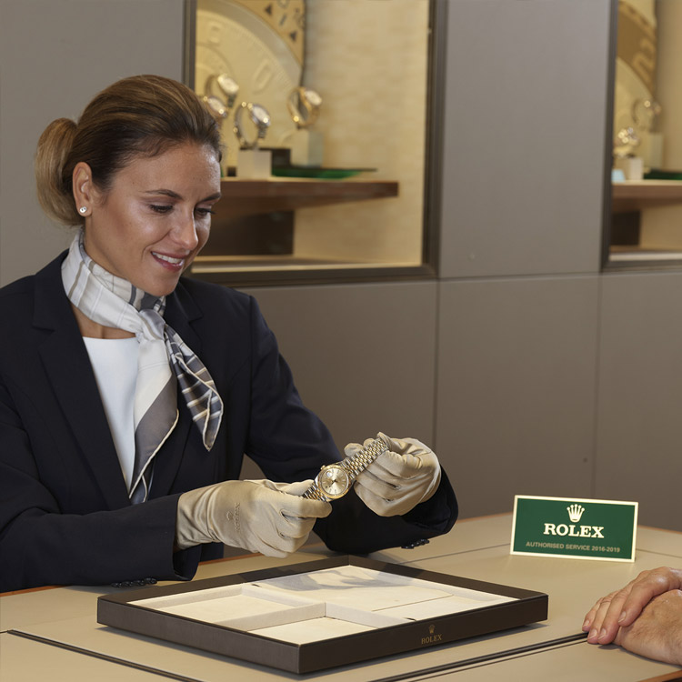 Eine Frau mit goldenen Handschuhen präsentiert einem Kunden im Rolex Corner eine Uhr