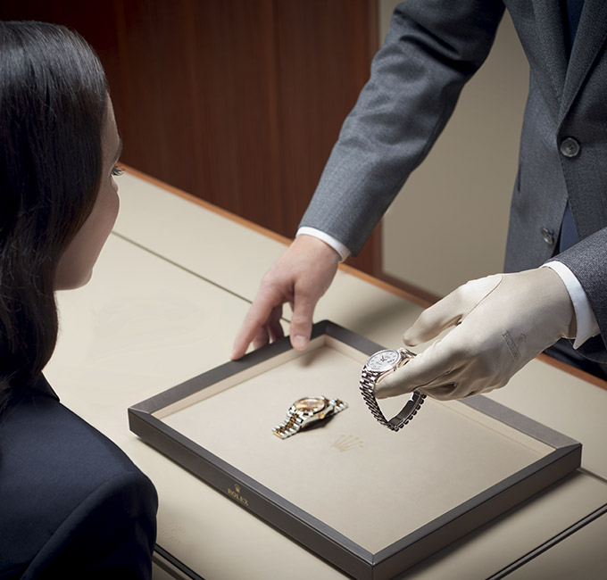 Eine Rolex Uhr wird einer Frau von einem Mann mit Handschuhen vorgeführt